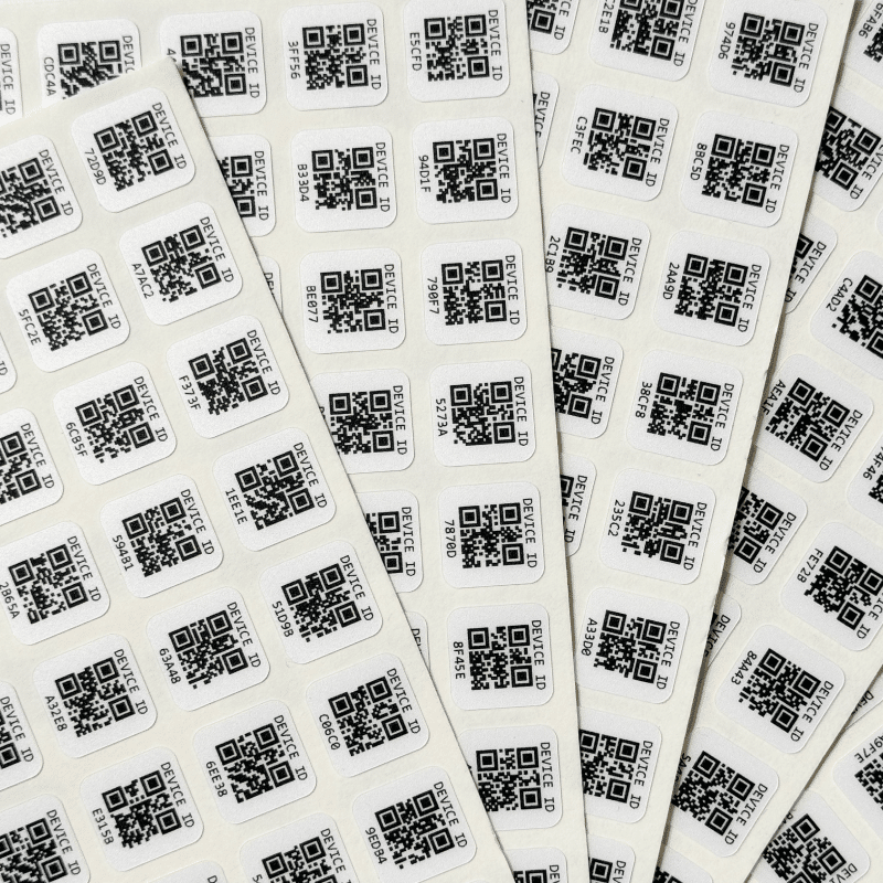 Sheets of QR code stickers are arranged in a fan-like pattern. Each sticker features a black QR code and a unique numerical code below it. The QR codes are placed on a white background, creating a contrasting and easily readable design.