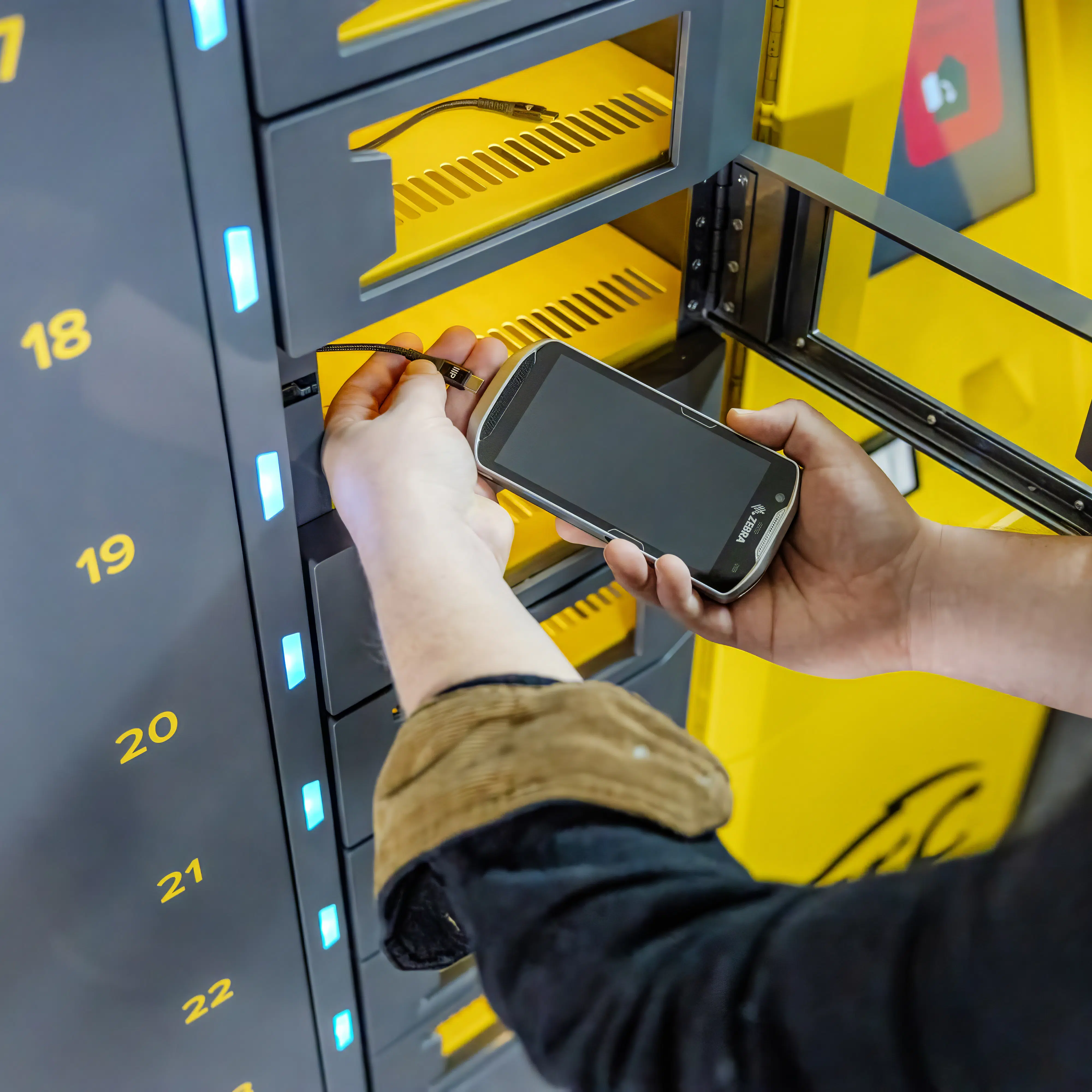 Employee placing a Zebra handheld device into a numbered charging locker at an ARC smart kiosk.