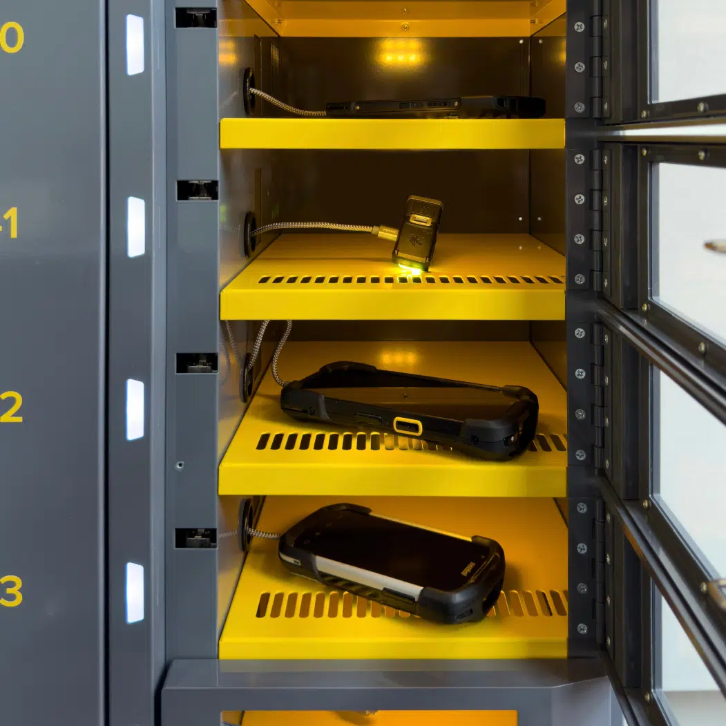 Close-up of open ARC kiosk locker bays with assortment of handheld enterprise devices securely charging inside numbered compartments.